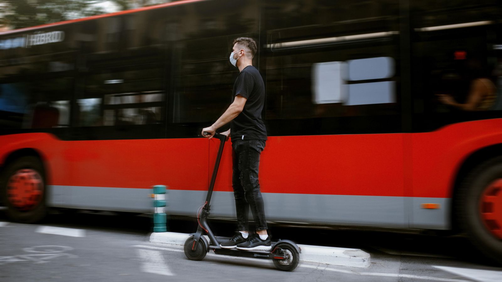 Un jove circula amb un patinet elèctric al costat d'un autobús, en una imatge d'arxiu
