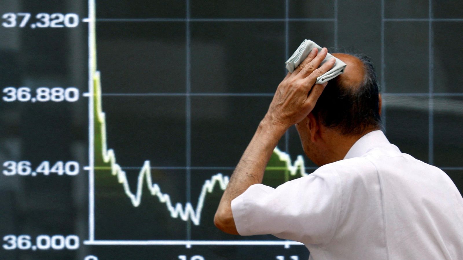 Un home observa una pantalla que mostra la caiguda en la borsa japonesa