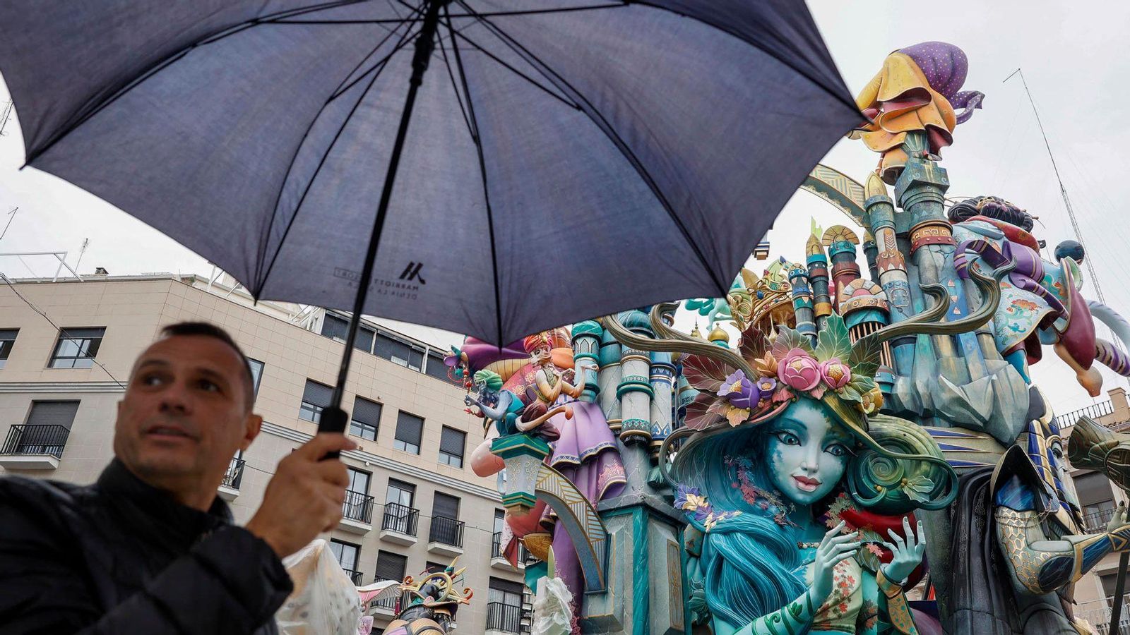 Un home es cobreix amb un paraigua davant del monument de la Falla del Convent de Jerusalem
