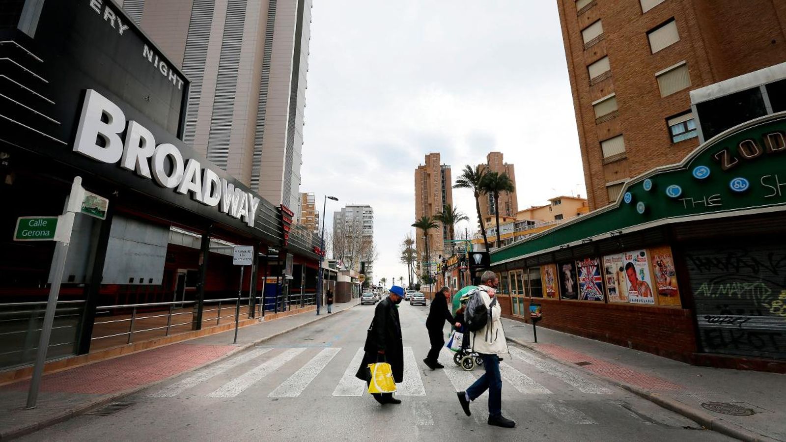 Diversos vianants creuen un carrer de Benidorm, amb nombrosos locals d'oci tancats