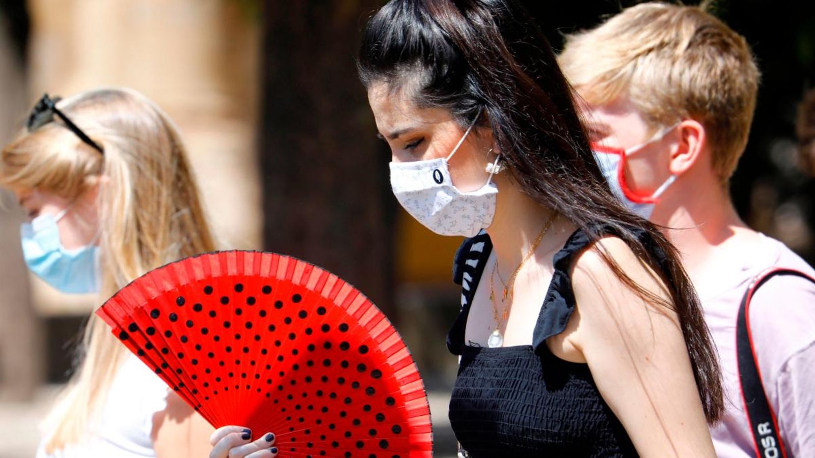 Diverses persones amb mascaretes i ventall caminen per un carrer de Còrdova
