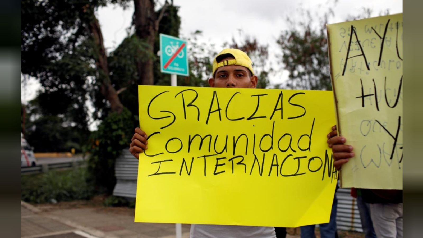 Un home sosté una pancarta prop d'un magatzem on es guarda l'ajuda humanitària per a Veneçuela