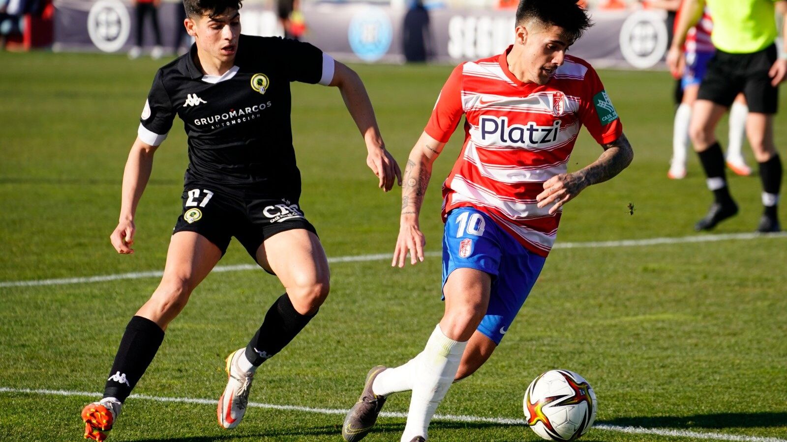 Un jugador del filial del Granada condueix la pilota davant la mirada de l'herculà