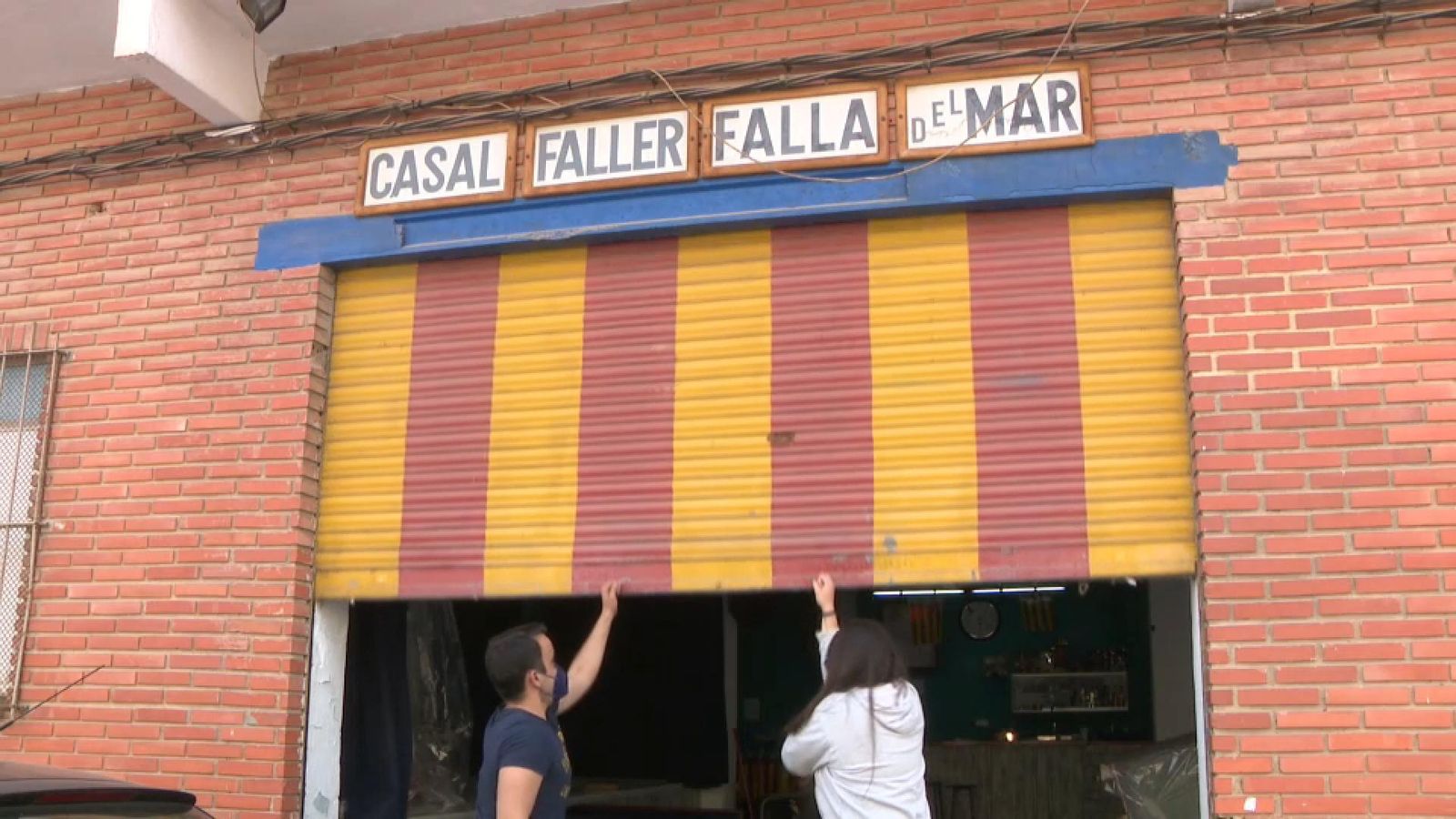 Dos integrants d'una comissió fallera baixen la persiana d'un casal