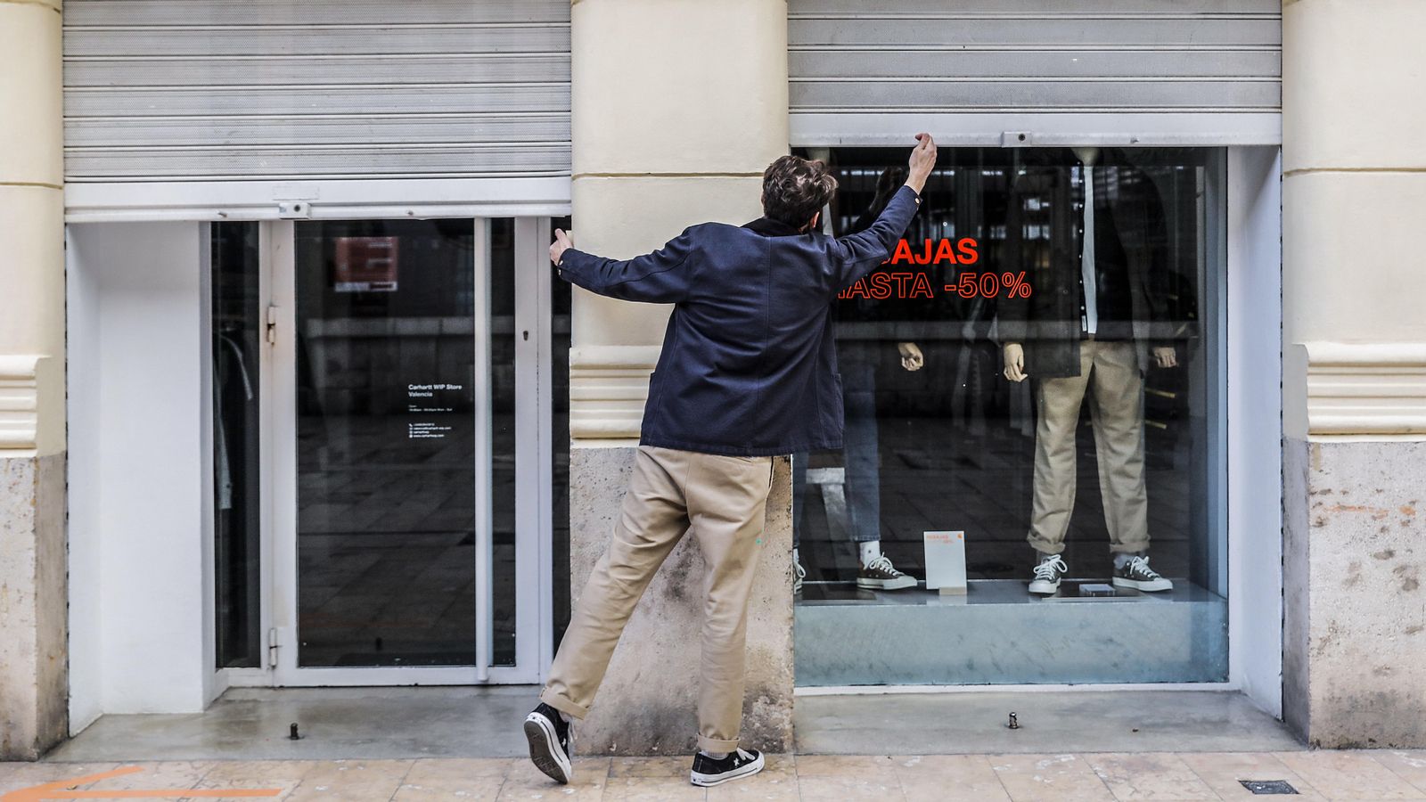 Un treballador baixa la persiana d'un local comercial, en una imatge d'arxiu