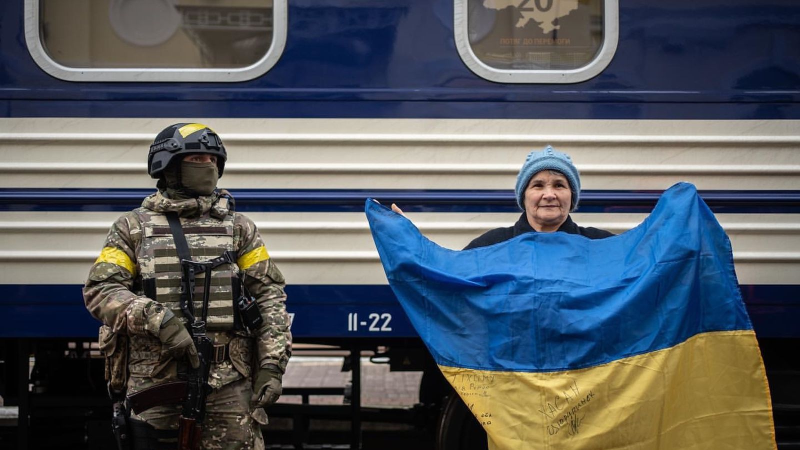 Una dona sosté una bandera al costat d'un soldat en la celebració del Dia del ferrocarril a Ucraïna