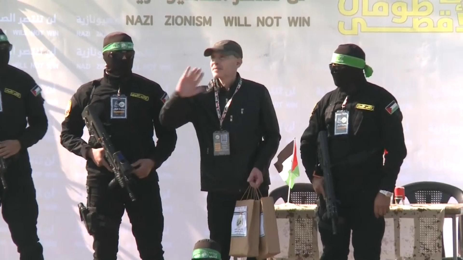 Entrega del tercer ostatge, Keith Siegel, amb un cartell al darrere en què es pot llegir el missatge: 'El siononisme nazi mai guanyarà"