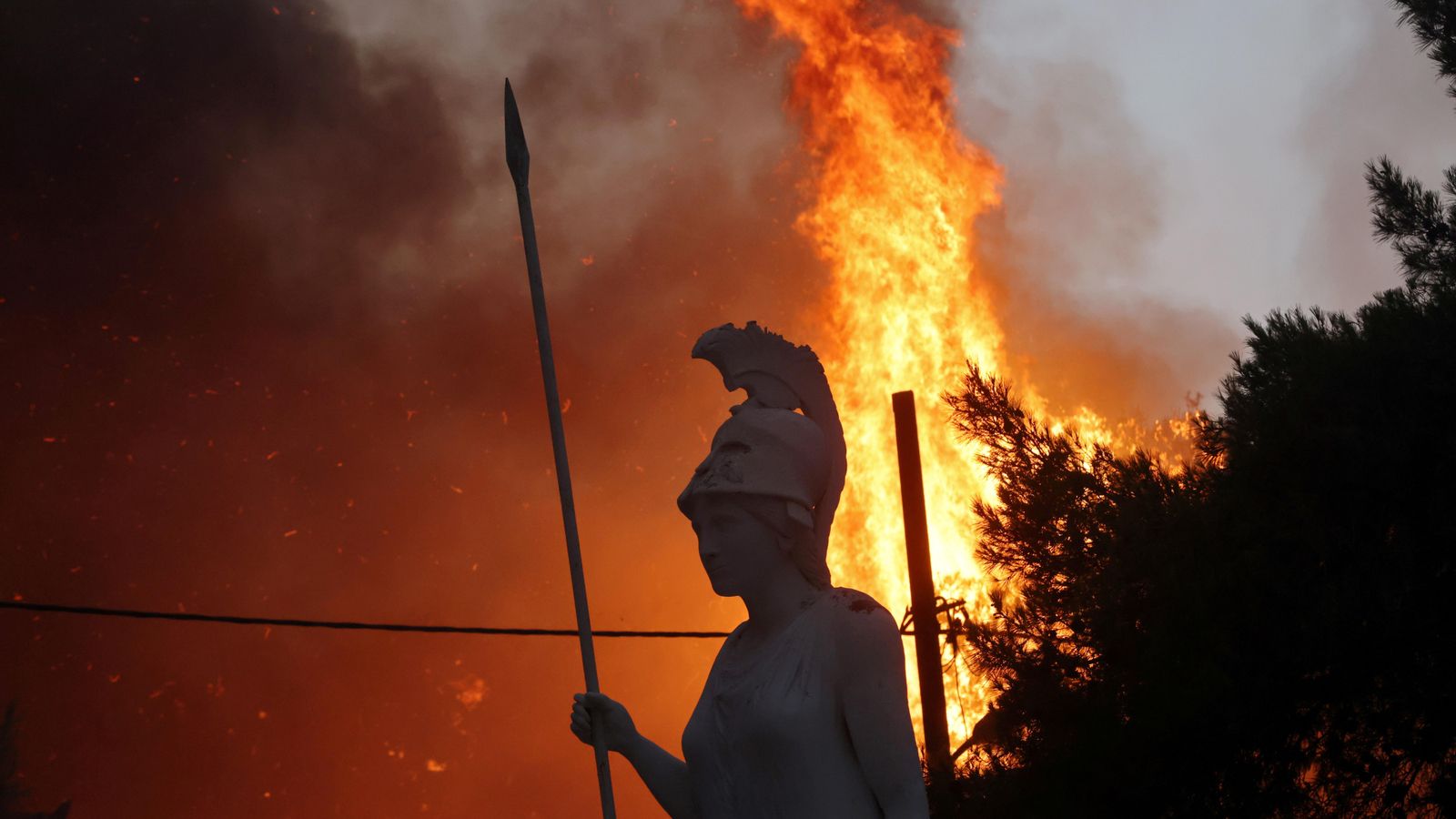 Una estàtua de la deesa Atenea amb les flames del suburbi de Varibombi de fons