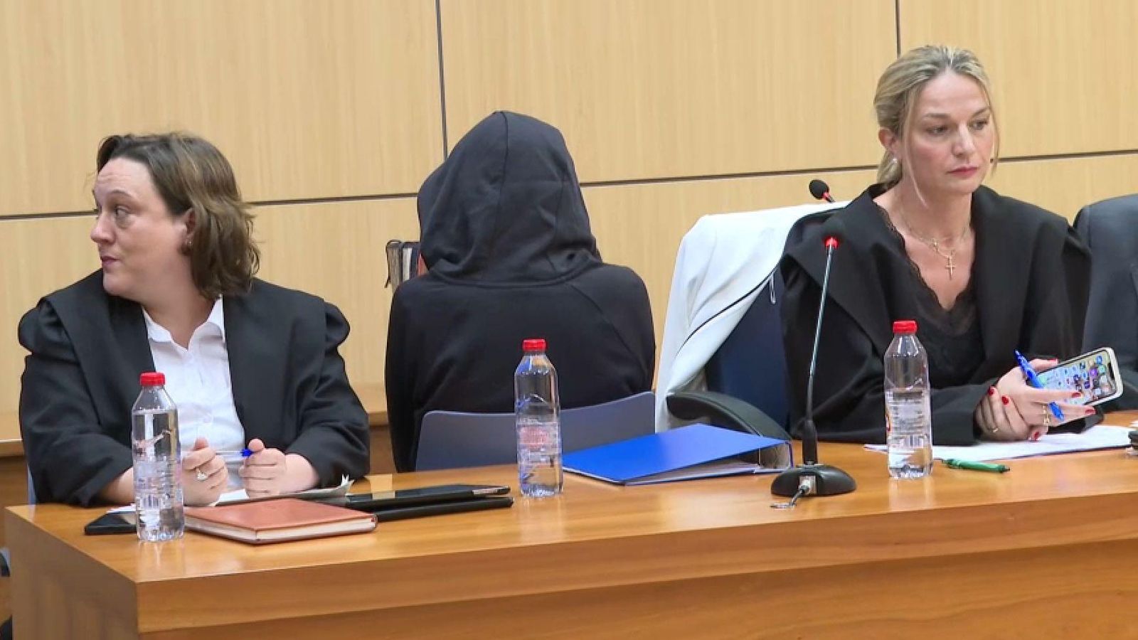 L'assassina confessa, amb el rostre ocult amb una caputxa, al costat de les seues advocades