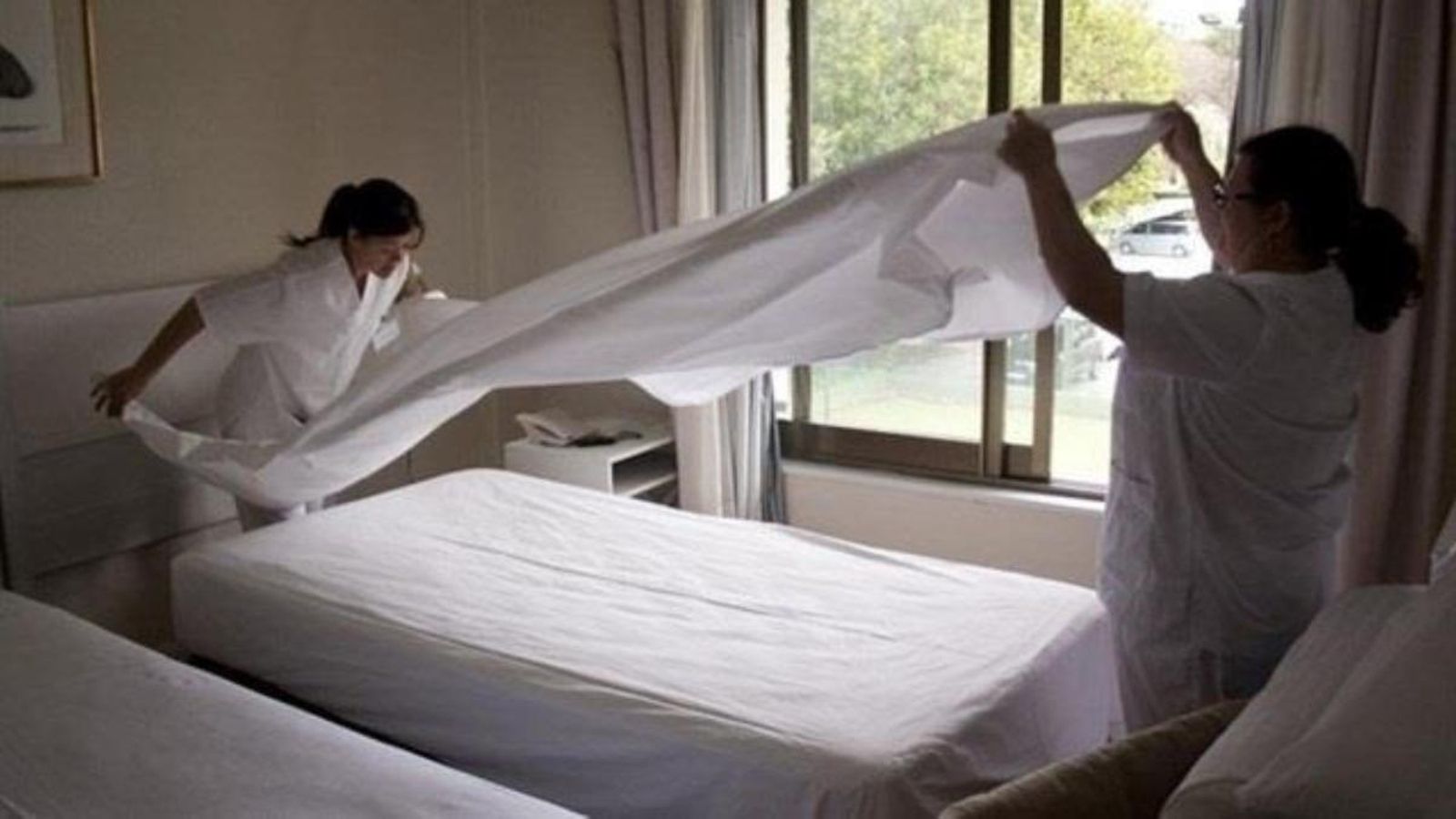 Dos cambreres de pis fent el llit d'un establiment hoteler en una imatge d'arxiu